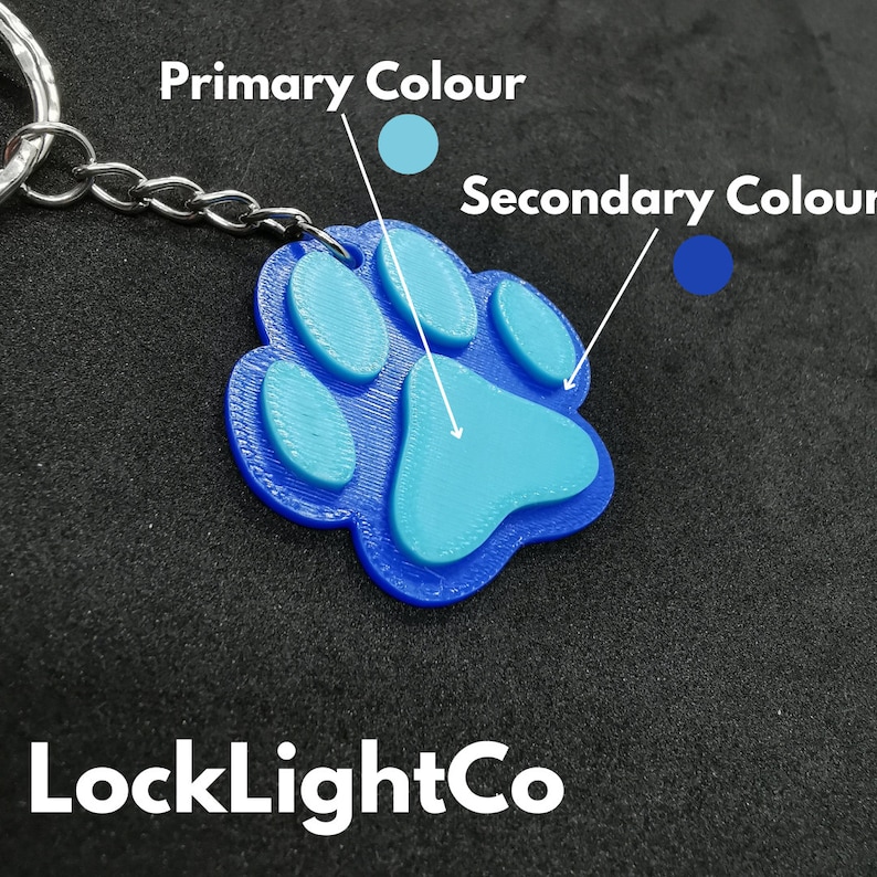 May include: A blue paw print keychain with a light blue paw print design. The keychain is attached to a silver chain.