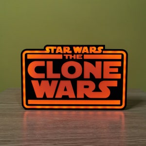 以下が含まれることがあります： 「スター・ウォーズ クローン・ウォーズ」と書かれた黒とオレンジの光る看板です。