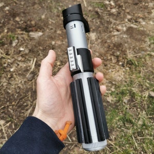 May include: A black and silver lightsaber toy with a black handle and a silver blade. The blade has black stripes and a silver tip. The handle has a black button and a silver switch.