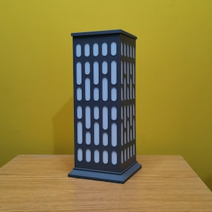 May include: A gray table lamp shaped like a tall building with a white geometric pattern.