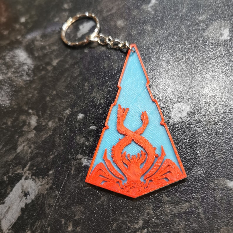 May include: A blue and orange 3D printed keychain shaped like a triangle with a crab design inside.