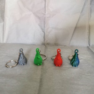 May include: Four gnome keyrings in different colours: grey, green, red, and blue. Each keyring has a silver ring and a small gnome figure.