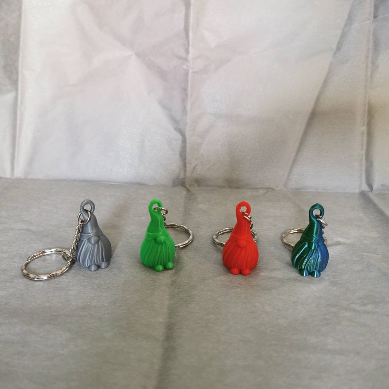 May include: Four gnome keyrings in different colours: grey, green, red, and blue. Each keyring has a silver ring and a small gnome figure.