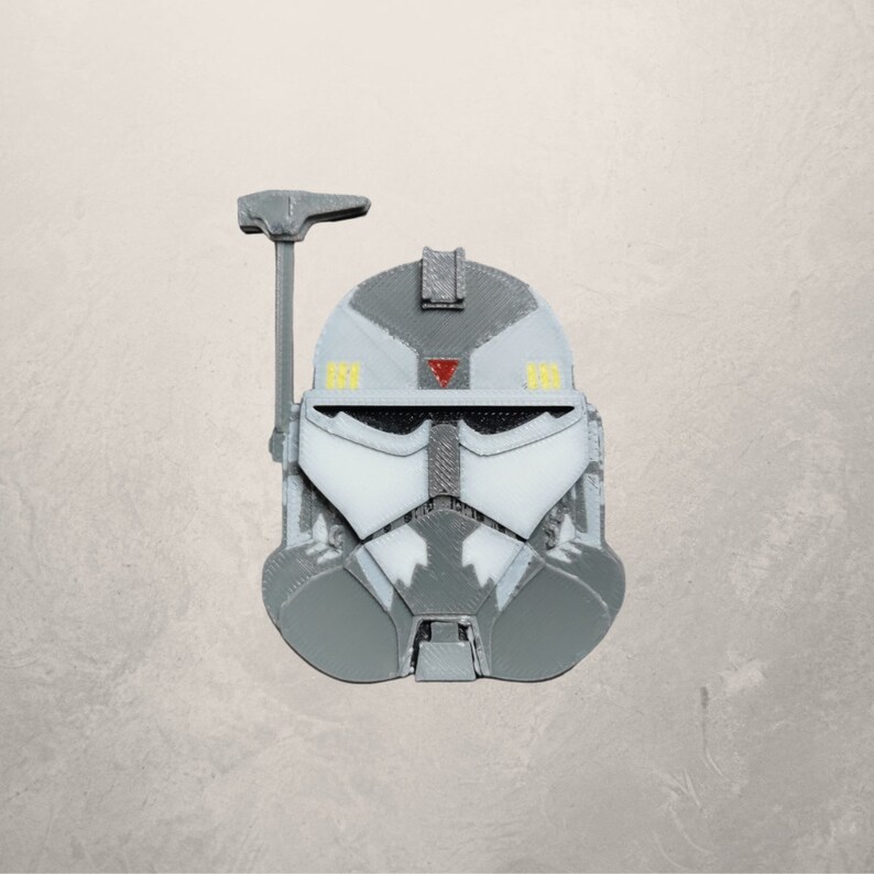 May include: A gray and white plastic helmet with a red triangle and yellow accents. The helmet has a visor and a small antenna on top.