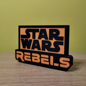 May include: Black and orange sign with the text "Star Wars Rebels" in a bold, blocky font.