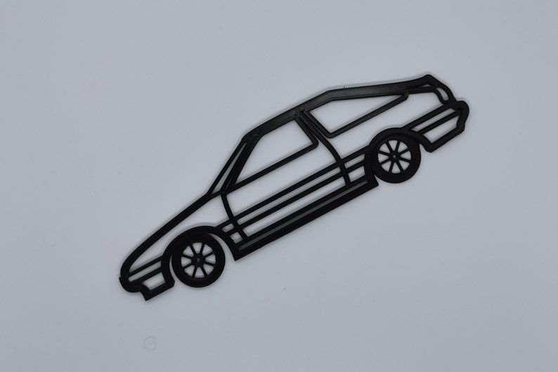 May include: Black outline of a station wagon car with visible wheels and windows. The car is angled diagonally against a white background. The wheels have a star-like design.