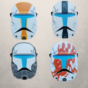 May include: Four different colored plastic helmets with a blue visor. The helmets are white with different colored designs. One helmet is orange, one is black and white, one is gray, and one is orange and white.