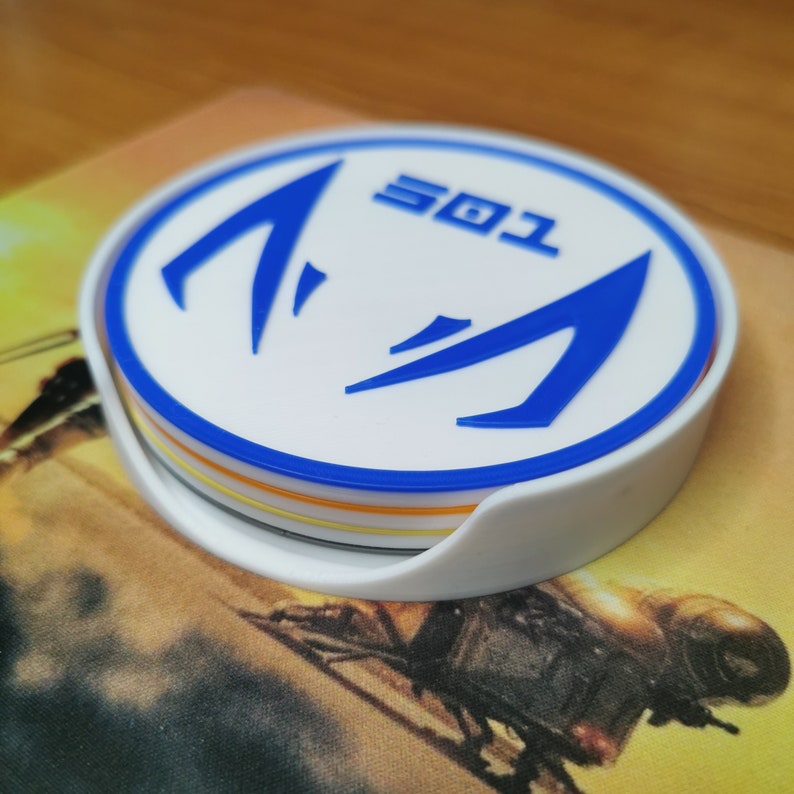 Puede incluir: Un posavasos blanco con un dise&ntilde;o azul que presenta dos flechas estilizadas y el texto "501". El posavasos est&aacute; hecho de m&uacute;ltiples capas de diferentes colores.