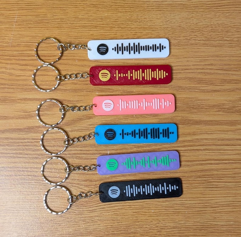 May include: Six colorful keychains with a Spotify logo and a barcode design. The keychains are white, red, pink, blue, purple, and black.