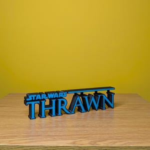 May include: A black and blue 3D printed sign that reads "STAR WARS THRAWN".