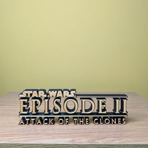 May include: A black and gold 3D printed sign that reads "STAR WARS EPISODE II ATTACK OF THE CLONES".