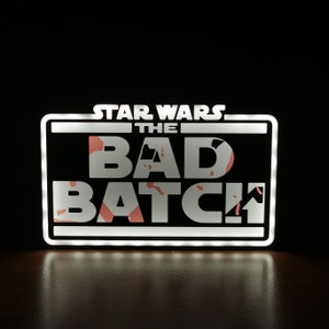 May include: A white light-up sign with the text "STAR WARS THE BAD BATCH" in white letters with a pink and orange splatter pattern behind the letters.