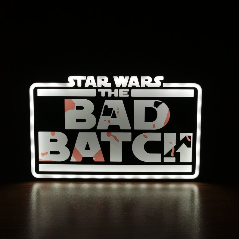 May include: A white light-up sign with the text "STAR WARS THE BAD BATCH" in white letters with a pink and orange splatter pattern behind the letters.