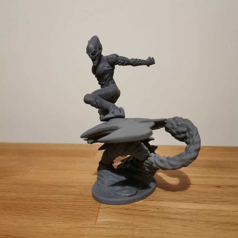 May include: A gray 3D printed figurine of a female character with a scorpion tail and wings. The character is posed in a dynamic action pose with one leg raised and arms outstretched.