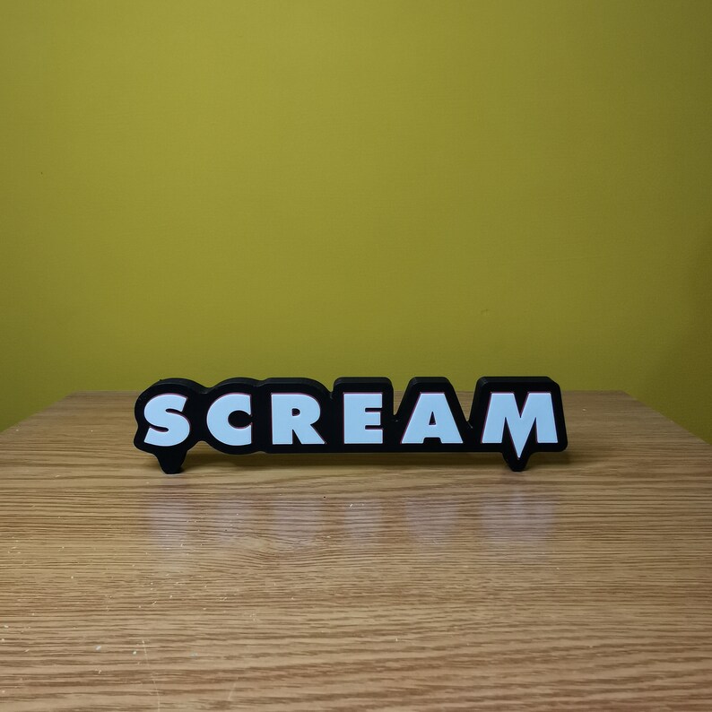 May include: Black and white "SCREAM" sign with a red outline. The sign is made of a thick, durable material and has a slightly raised surface.