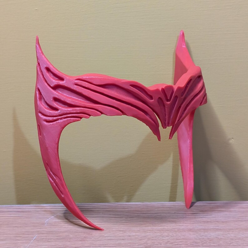 May include: A red plastic headband with a detailed, textured design. The headband is curved and has two pointed ends.