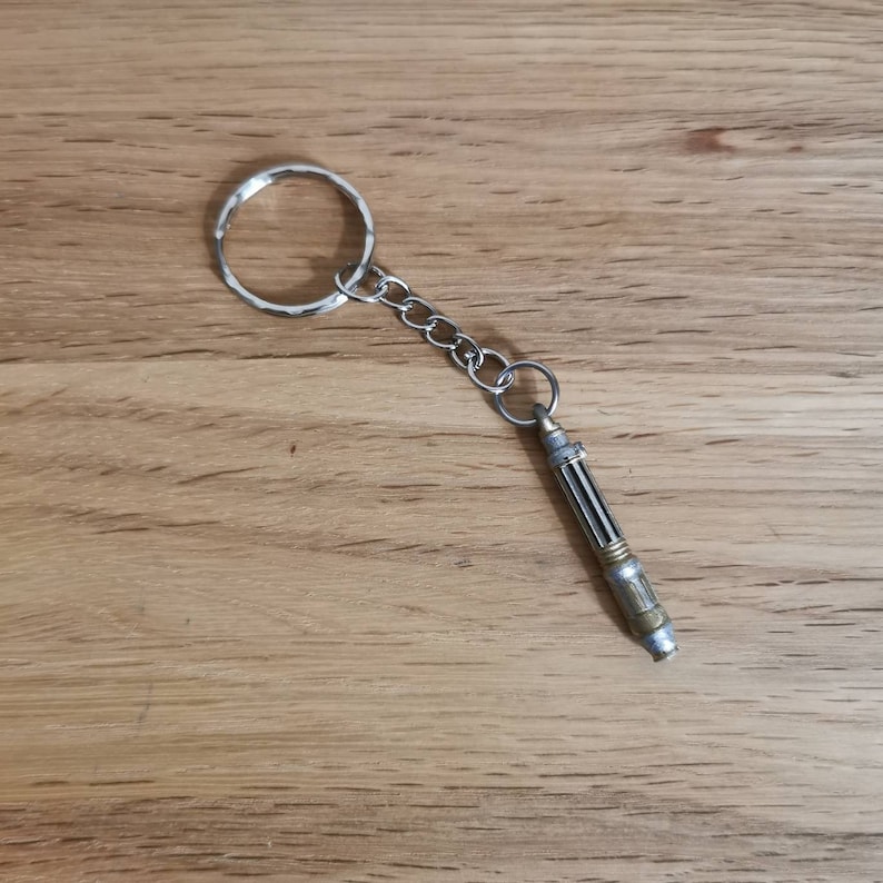 Op de afbeelding: Een zilveren sleutelhanger met een zilveren en gouden replica van de sonic schroevendraaier van de Doctor.