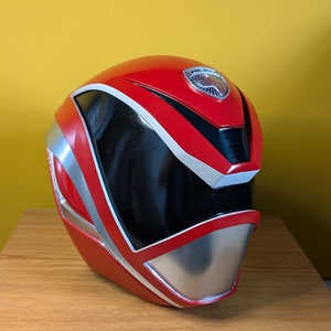 May include: Red and silver Power Ranger helmet with a black visor and a silver emblem on the top.