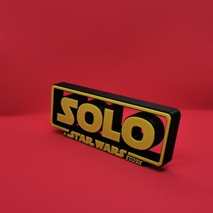 May include: Black and yellow 3D printed sign with the text "SOLO: A STAR WARS STORY".