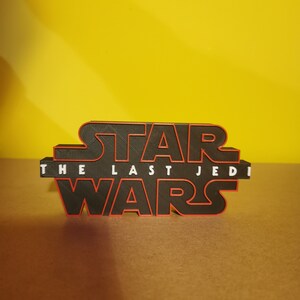 May include: A black 3D printed Star Wars logo with red outlining. The text "The Last Jedi" is printed in white below the logo.