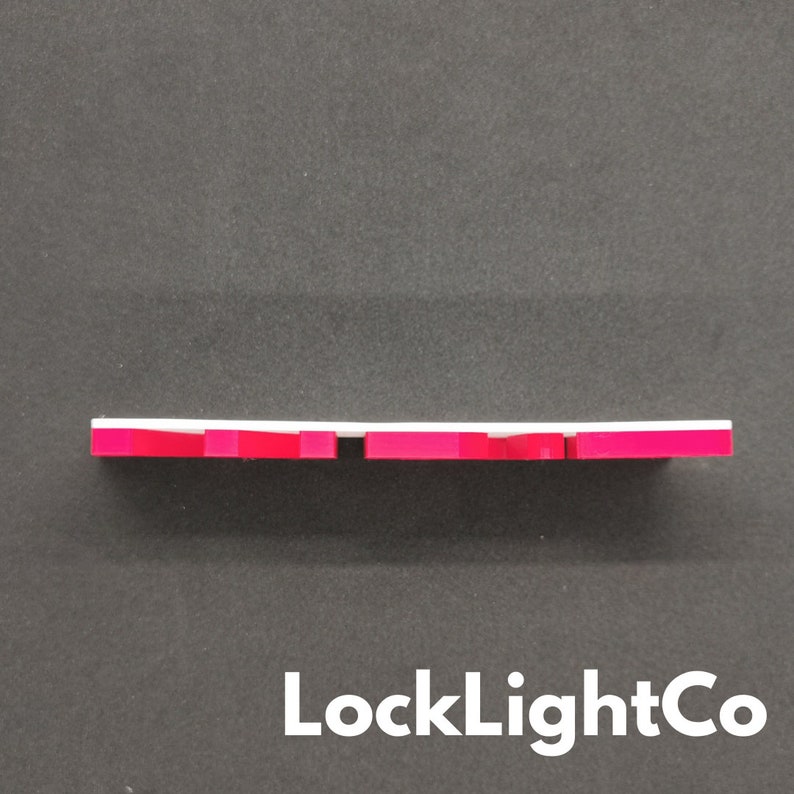 Op de afbeelding: Een wit en rood rechthoekig object met een reeks rode blokken langs de onderrand. Het object staat tegen een donkergrijze achtergrond. De tekst "LockLightCo" staat onderaan.