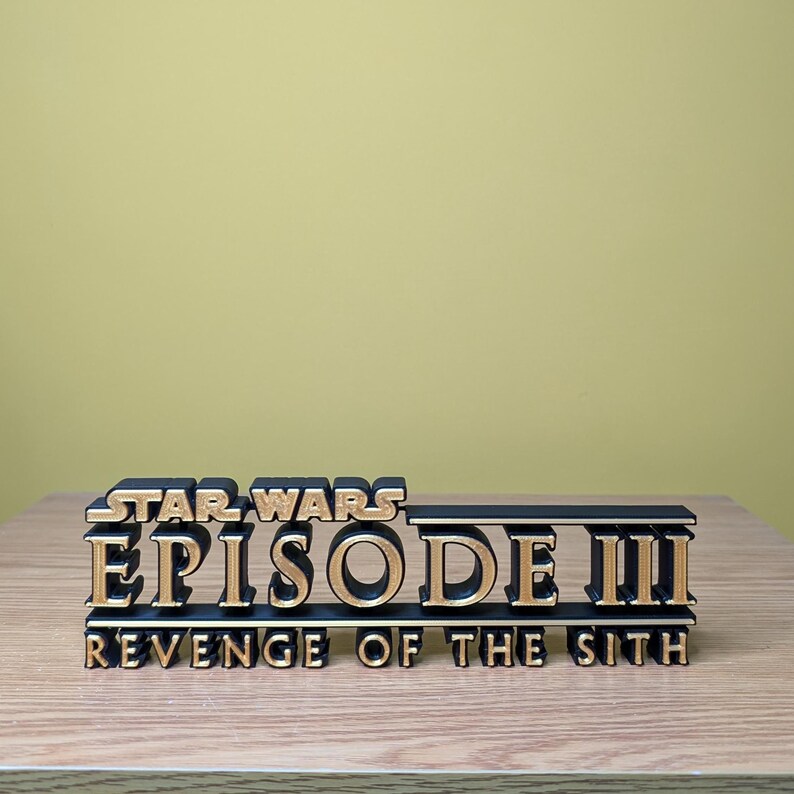May include: A black and gold 3D printed sign that reads "Star Wars Episode III Revenge of the Sith".