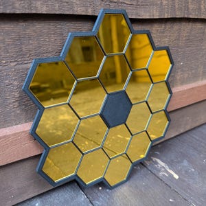May include: A black and gold honeycomb-shaped mirror with a central black hexagon. The mirror is made of multiple small hexagonal mirrors.
