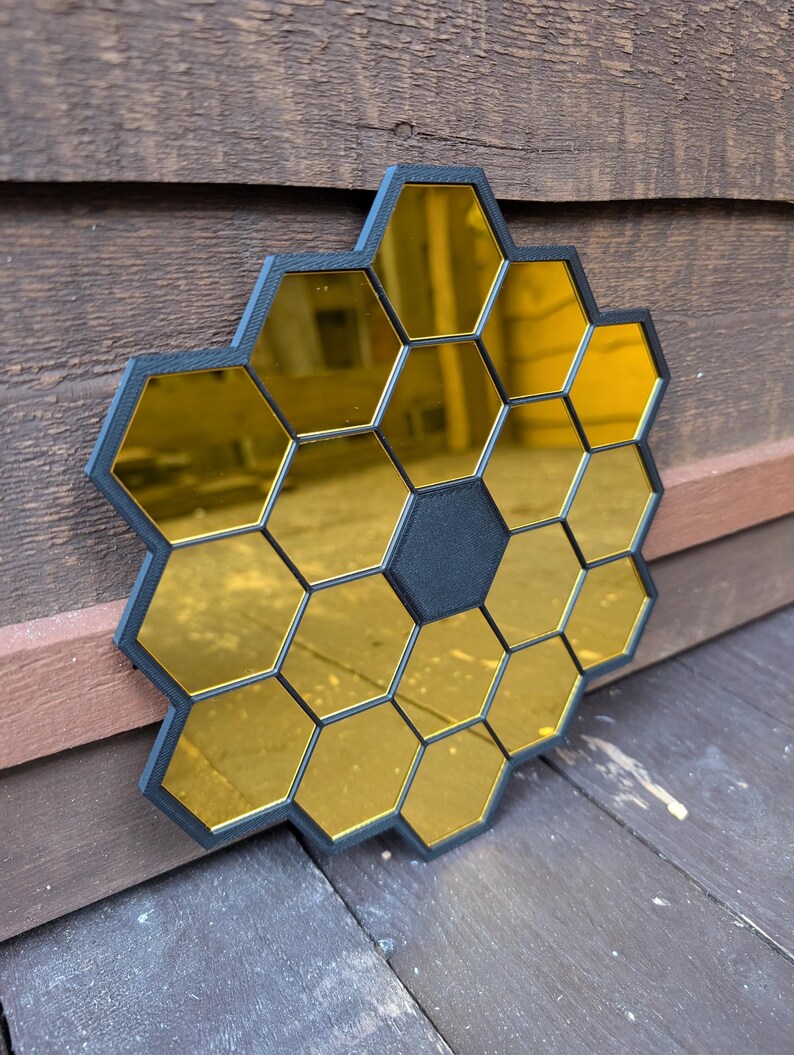 May include: A black and gold honeycomb-shaped mirror with a central black hexagon. The mirror is made of multiple small hexagonal mirrors.