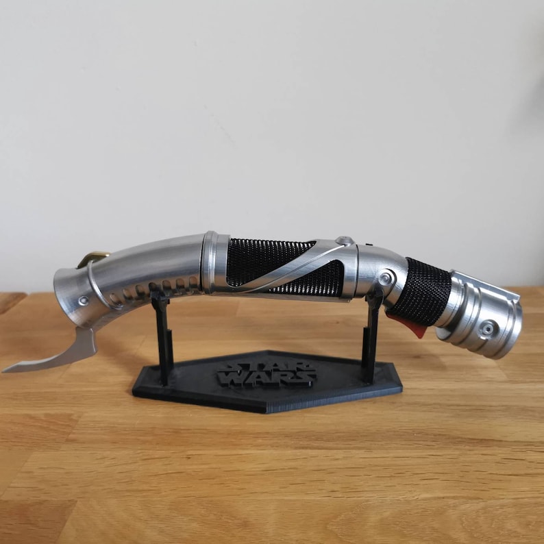 May include: A silver and black lightsaber with a curved handle and a black stand with the words "Star Wars" printed on it.