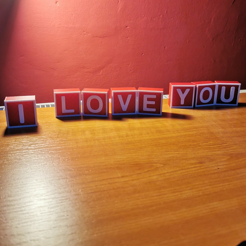 May include: Red wooden blocks spelling out the phrase "I LOVE YOU" on a wooden surface.