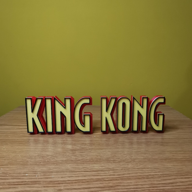 Pu&ograve; includere: Lettere di plastica rosse e nere che compongono la scritta "KING KONG" su una superficie di legno.