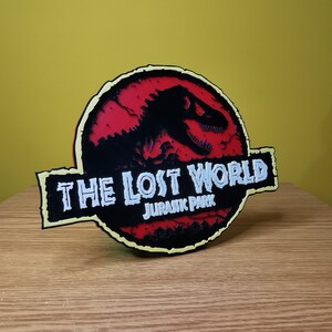 May include: A red, black, and yellow 3D printed sign with the text "The Lost World Jurassic Park" and a silhouette of a dinosaur.