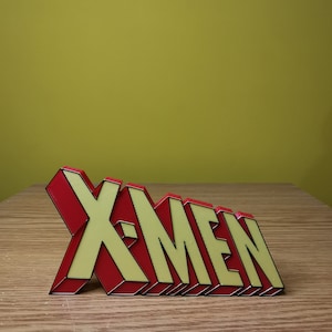 K&ouml;nnte beinhalten: Ein rotes und gelbes 3D-Plastikschild mit der Aufschrift "X-Men".