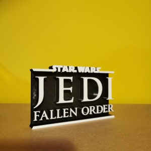 May include: A black and white 3D printed sign with the text "STAR WARS JEDI FALLEN ORDER".