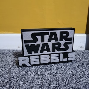 May include: Black and silver 3D printed sign with the text "STAR WARS REBELS".