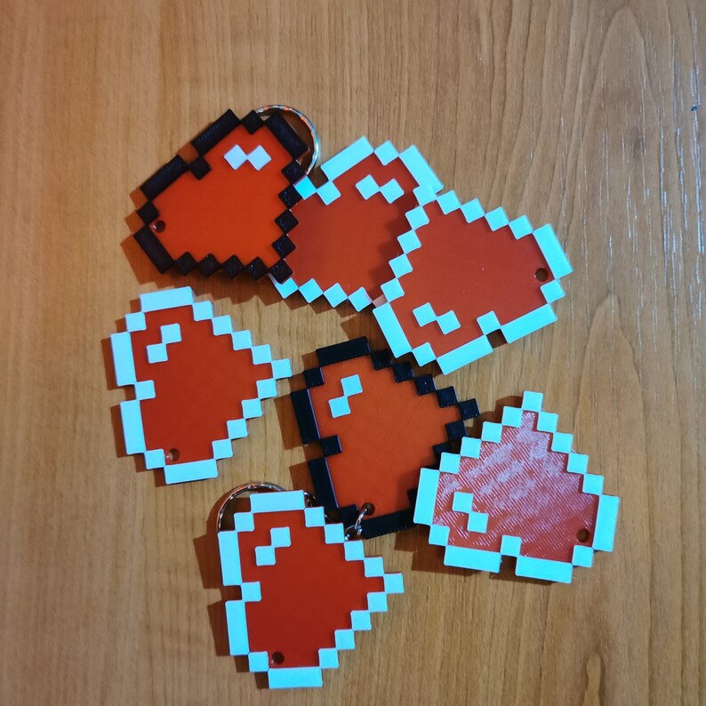 May include: Six red pixel heart-shaped keychains with a light blue border. The keychains are made of plastic and have a black metal ring.