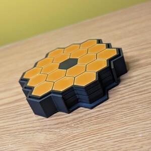 May include: A stack of black and orange honeycomb-shaped coasters. The coasters are made of a 3D printed material.