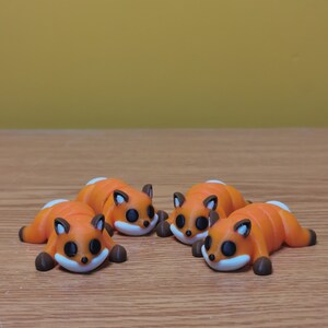 May include: Four small orange and brown figurines of foxes lying on their bellies. The foxes have black eyes and white accents on their faces.