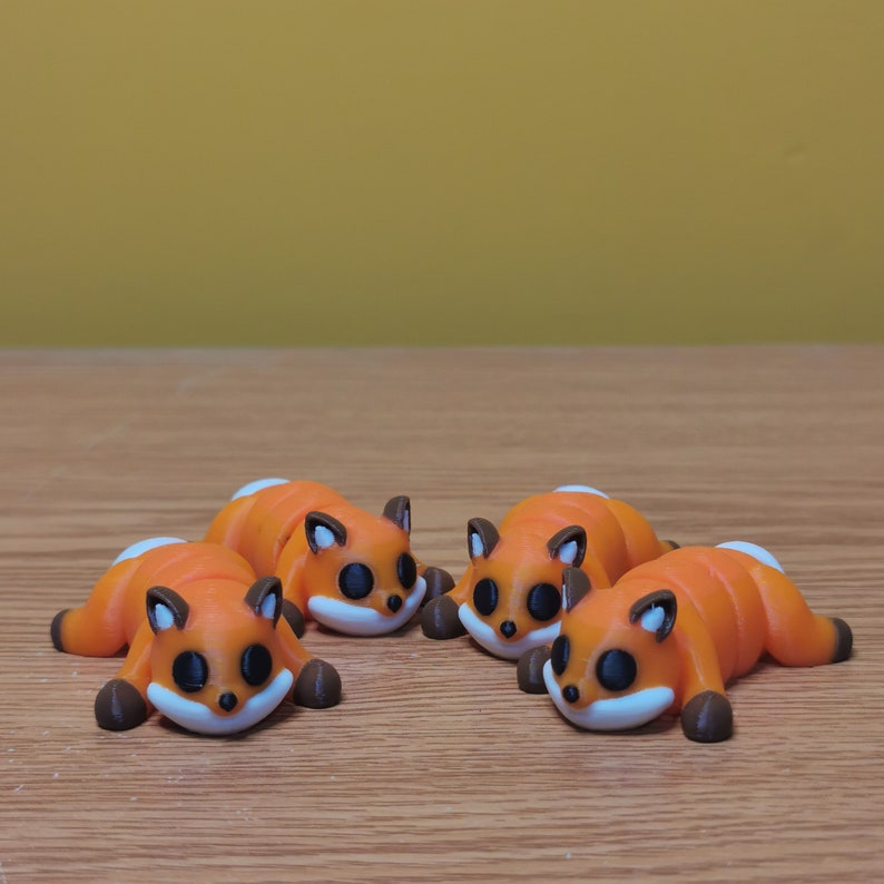 May include: Four small orange and brown figurines of foxes lying on their bellies. The foxes have black eyes and white accents on their faces.