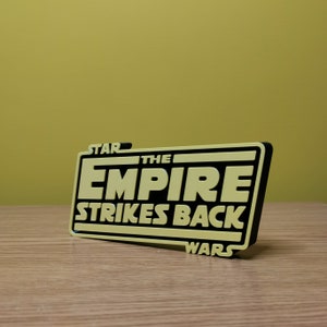 May include: A yellow and black 3D printed sign that reads "Star Wars The Empire Strikes Back".