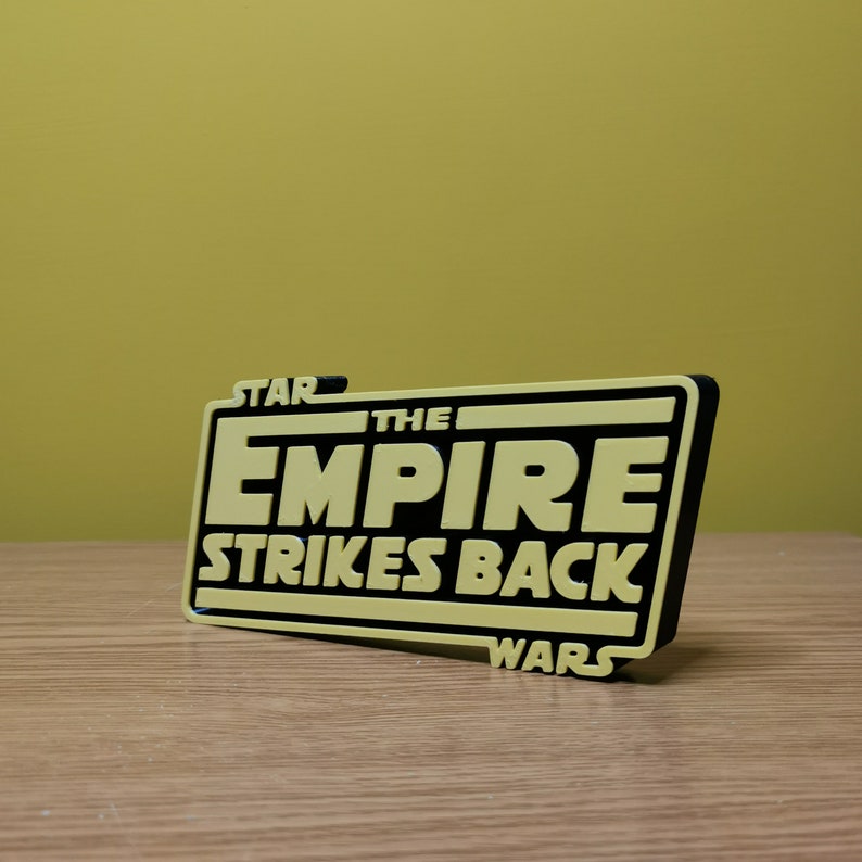 May include: A yellow and black 3D printed sign that reads "Star Wars The Empire Strikes Back".