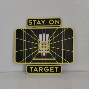 May include: A yellow and black target sign with the words "Stay On Target" above and "Target" below. The target is a black and white grid with a red and white stripe in the center.