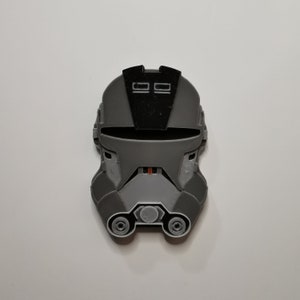 May include: A gray and black 3D printed helmet with a visor and two small rectangular details on the top.