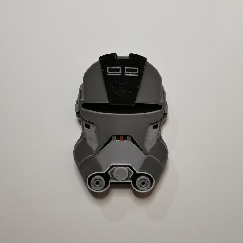 May include: A gray and black 3D printed helmet with a visor and two small rectangular details on the top.