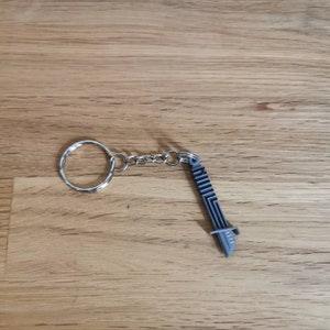 Op de afbeelding: Een zilveren sleutelhanger met een zilveren ring en een zilveren ketting bevestigd aan een grijze plastic zwaardbedel.