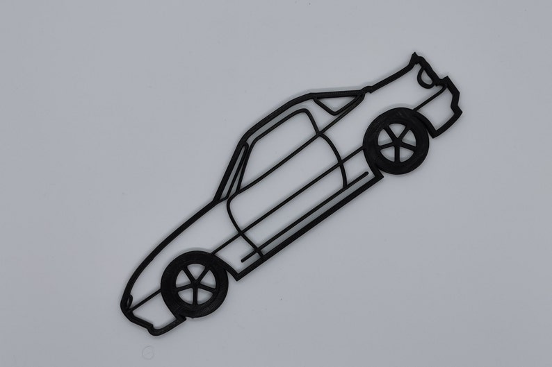 May include: A black line drawing of a sports car with a rounded roof and a spoiler. The car is facing to the right and is angled slightly upwards. The car has two doors and four wheels.