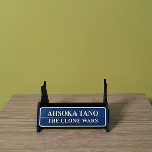 May include: A blue and black display stand with a sign that reads "Ahsoka Tano The Clone Wars".