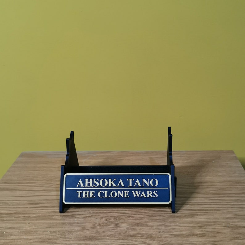 May include: A blue and black display stand with a sign that reads "Ahsoka Tano The Clone Wars".