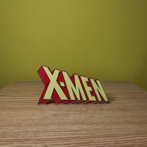 Puede incluir: Un letrero 3D rojo y amarillo que dice "X-MEN".