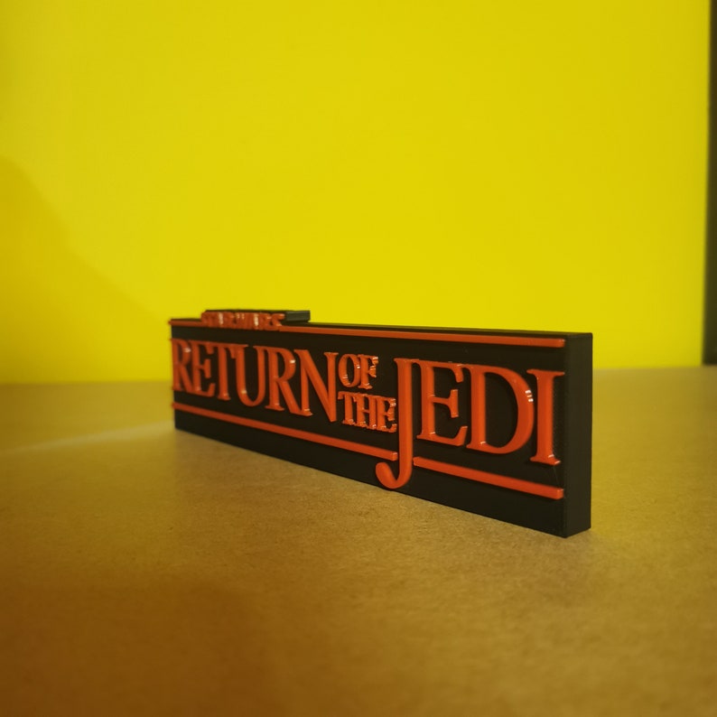 May include: A black and orange 3D printed sign that reads "STAR WARS RETURN OF THE JEDI".